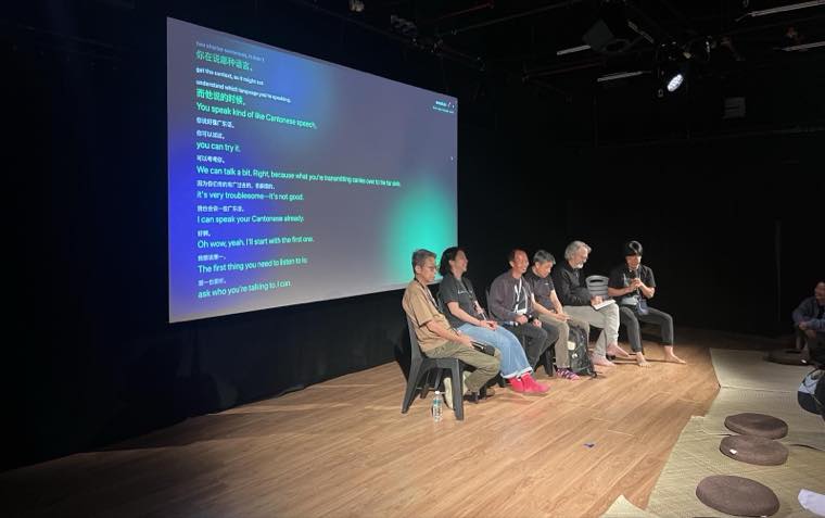 A real eventsub session: the big screen showing live bilingual captions in front of a seated panel
