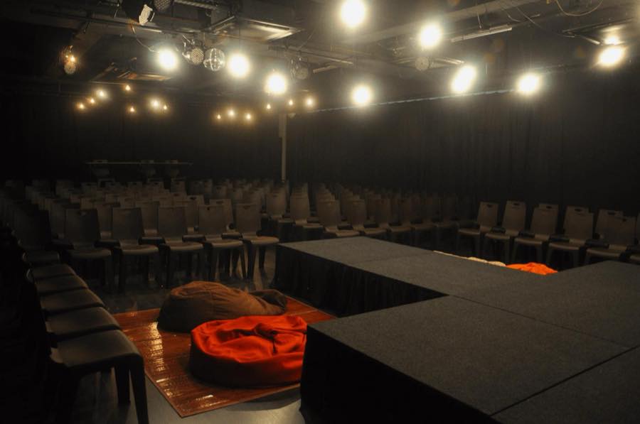 An empty black box theatre set up with rows of chairs and a low platform stage